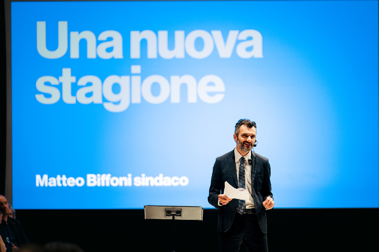 Matteo Biffoni sul palco durante l'apertura della campagna elettorale a sindaco di Prato, alla Camera di Commercio, il 23 aprile 2026. Sullo sfondo, una grande proiezione blu con la scritta 'Una nuova stagione - Matteo Biffoni sindaco'.
